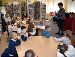 Pani pokazuje książkę dzieciom, które siedzą przy stolikach