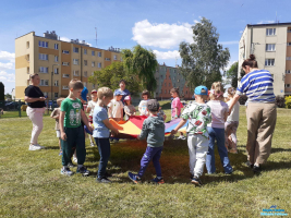 Dzieci trzymają koloworą chustę a obok nich stoją trzy Panie