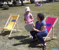 Pani siedzi na leżaku  i trzyma książkę, a obok stoi dziewczynka