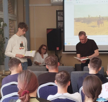 Pani siedzi a dwóch Panów stoi i trzyma książki