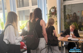 Grupa młodzieży stojąca w kolejce do stolika przy którym autorka podpisuje książki