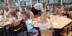 Dzieci siedzące przy dwóch stolikach i rysujące kredkami