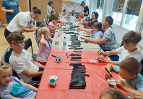 Duża grupa dzieci i osoby dorosłe ozdabiają filiżanki kolorowymi mazakami