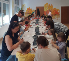 Duża grupa uczestników warsztatów siedzi  przy stole  i maluje mazakami filiżanki