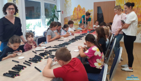 Przy stolikach siedzą dzieci, a obok dzieci stoją cztery panie