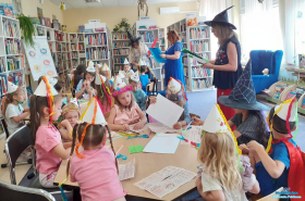 Dzieci siedzą przy stolikach a trzy kobiety stoją obok