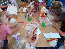 Na stoliku leżą kartki przy którym siedzą dzieci