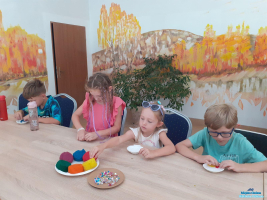 Grupa dzieci siedzi przy stoliku i wypełnia kolorową ciastoliną muszelkę gipsową