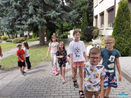 Grupa dzieci spaceruje z alpakami przy budynku biblioteki