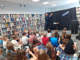 Pan pokazuje dłoń, a dzieci siedzą na dywanie