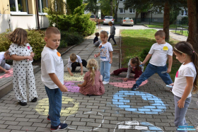 grupa dzieci stoi przed budynkiem i rysuje kolorowe kółka