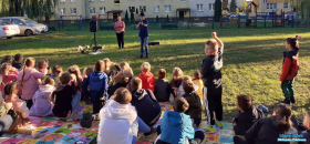 dzdwóch chłopców z podniesionymi rękami do góry. grupka siedzących dzieci na matach