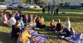 dzieci siedzą na kocach a w tle dorosłe osoby z dziećmi