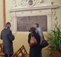 Trzy osoby dyskutując, stojąc przed epitafium w kościele