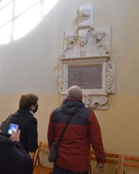 Trzy osoby oglądają epitafium w budynku kościoóła