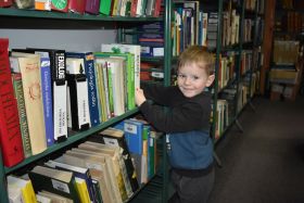 Mały chłopiec stoi przy półce z książkami