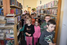 Grupa dzieci spaceruje między regałami z książkami