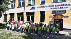 Grupa dzieci stoi przed budynkiem biblioteki