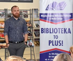 Wojciech Chmielarz na tle banneru reklamowego biblioteki